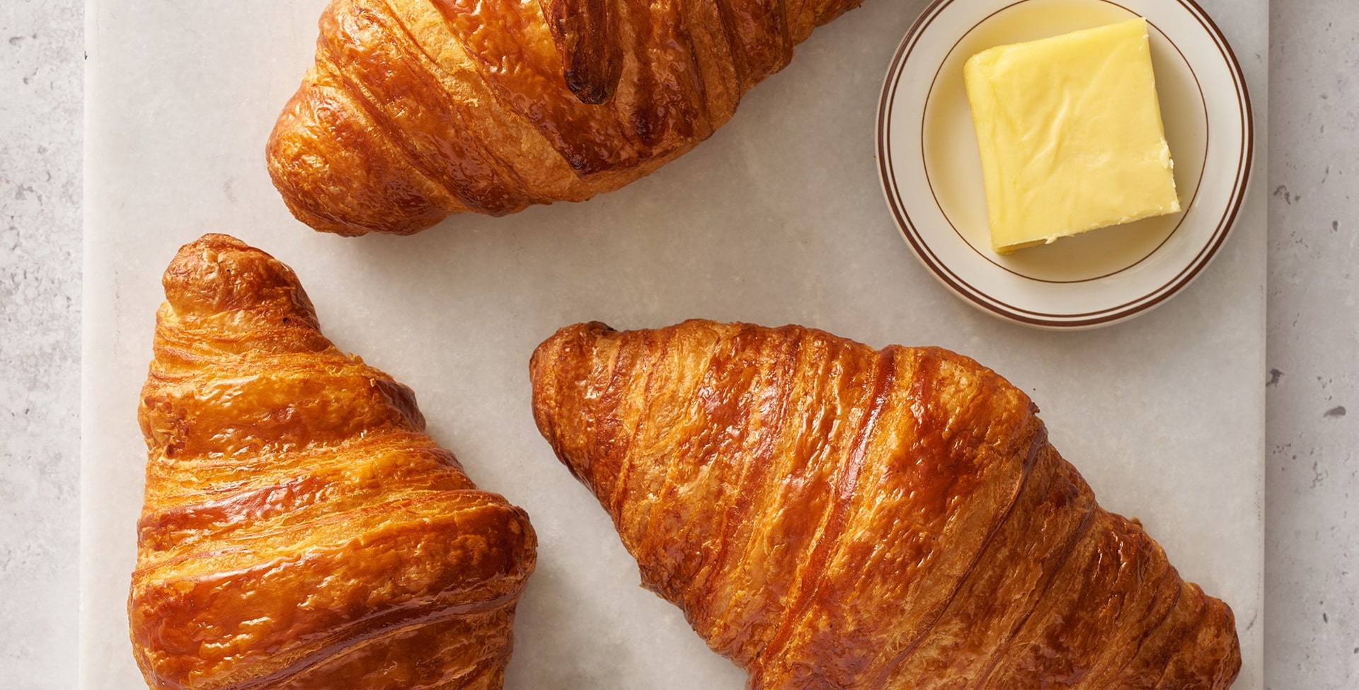 Trois croissants dorés et croustillants avec du beurre frais dans un bol en verre sur fond clair