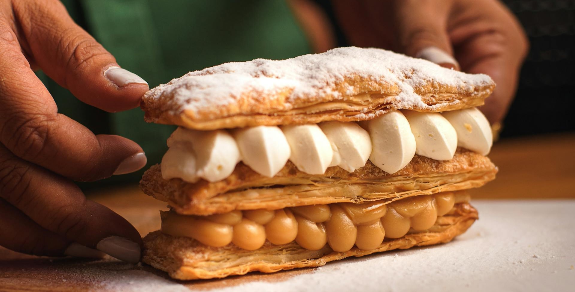Main tenant un éclair garni de crème pâtissière et de caramel, saupoudré de sucre glace