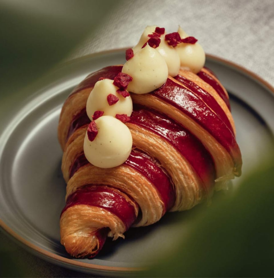 Croissant feuilleté garni de coulis rouge et surmonté de boules de mousse blanche parsemées de fruits rouges